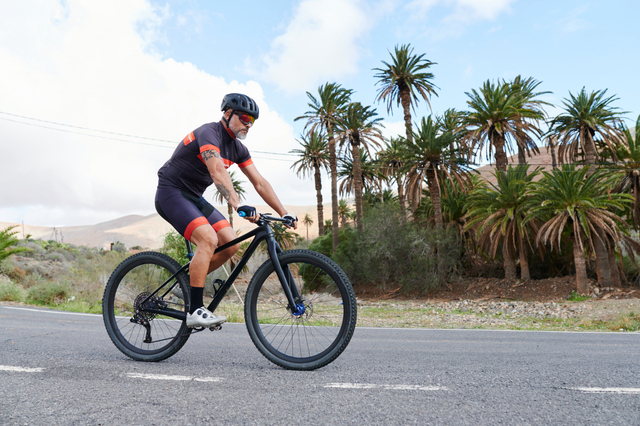 Fit mature man in cycling gear riding his mountain bike along a road through some scenic countryside