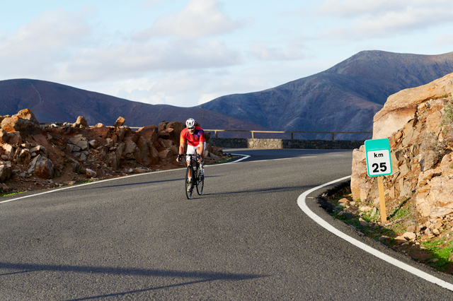 Fit mature man in cycling gear riding down a road through some scenic mountains in the summer