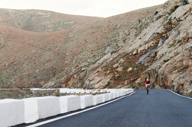 Fit man in cycling gear riding his bike up a road through scenic mountains in the summer